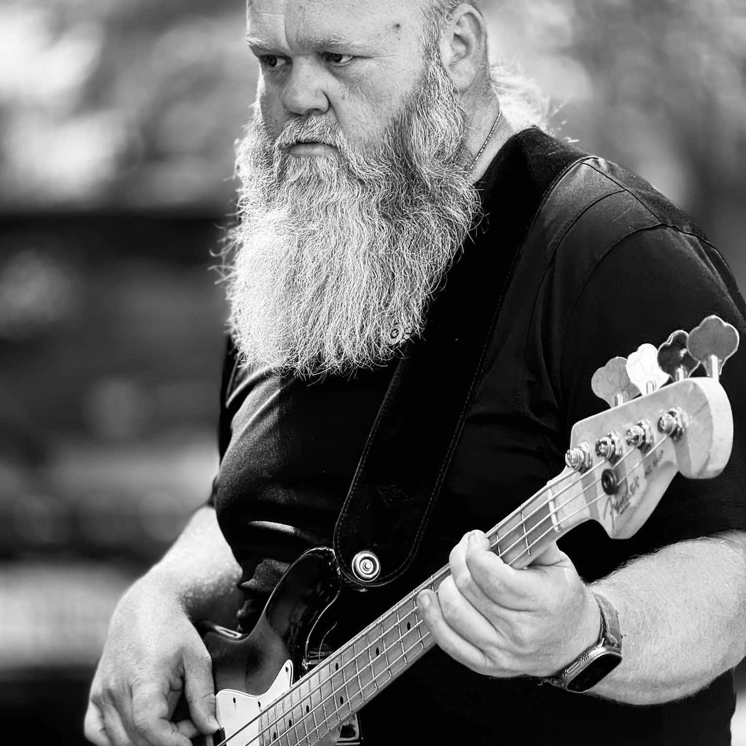 [ Founder name ], Founder & Steward, holding a Fender bass — black-and-white portrait