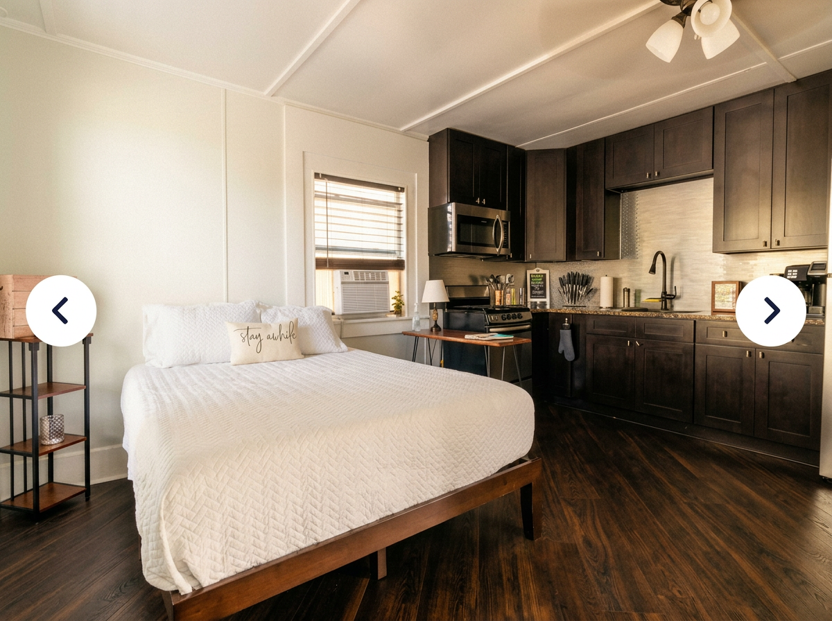 Wide shot of the studio: King bed on the left, full dark-cabinet kitchen with granite counters and stainless fridge on the right, all in one bright room