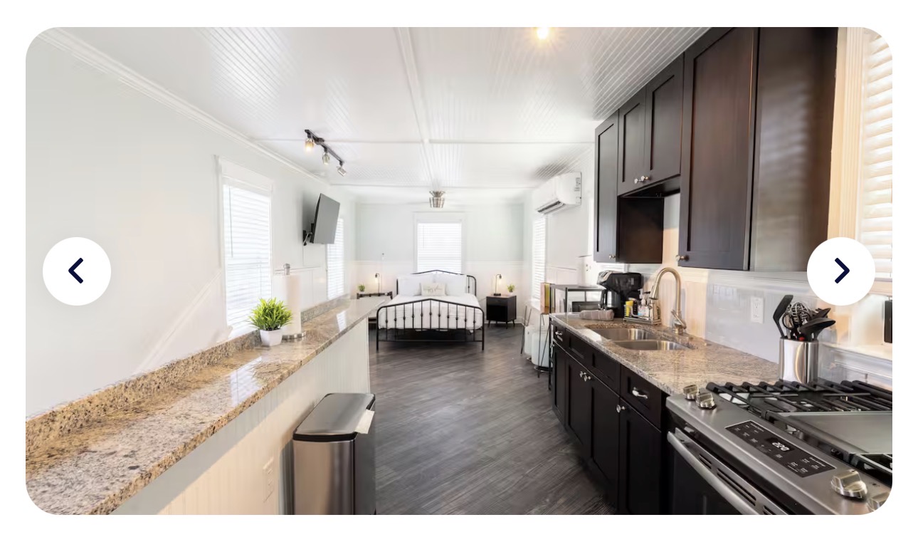 The Florida Room open-plan: granite galley kitchen on the right, Queen bed under wall-mounted TV in the distance, beadboard ceiling and soft sage walls